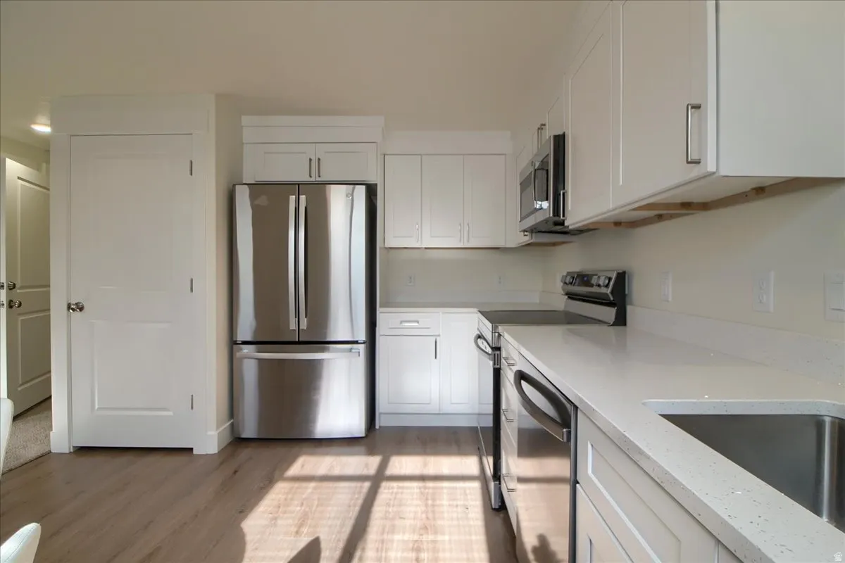Kitchen featuring light wood-finish flooring, white cabinetry with brushed nickel hardware, light-colored countertops, and stainless steel appliances including a refrigerator, range, microwave, and dishwasher