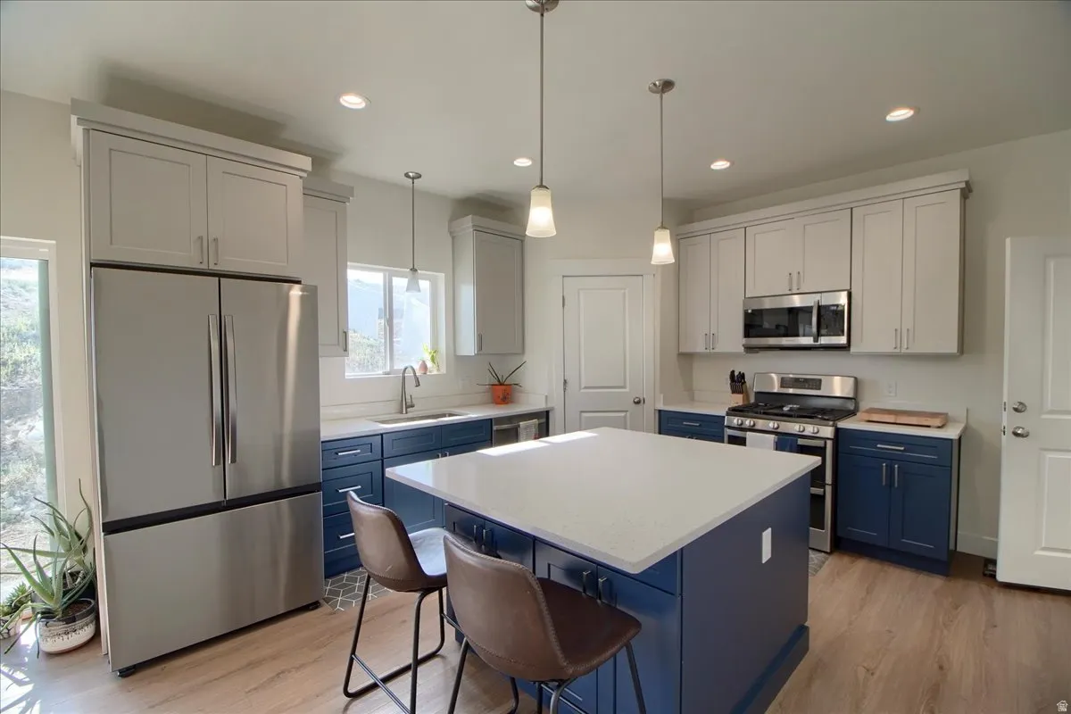 Modern kitchen featuring a large central island with a light-colored countertop, stainless steel appliances, two-tone cabinetry, recessed lighting, and wood-finish flooring