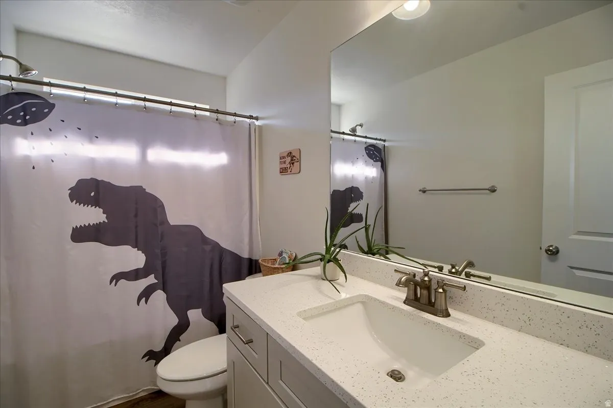 Bathroom featuring a spacious vanity with an integrated sink, a speckled countertop, a large wall-mounted mirror, and a shower with a chrome showerhead