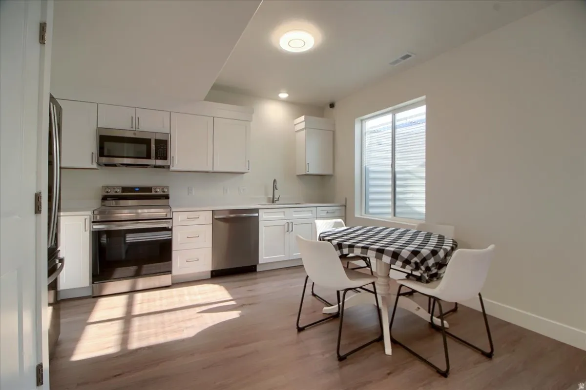 Contemporary kitchen featuring stainless steel appliances, white cabinetry, light-toned countertops, and wood-finish flooring