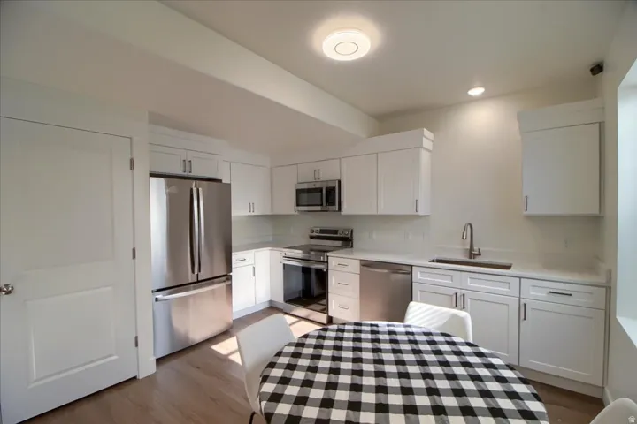 Contemporary kitchen featuring white cabinetry, stainless steel appliances, light-toned countertops, subway tile backsplash, and wood-finish flooring