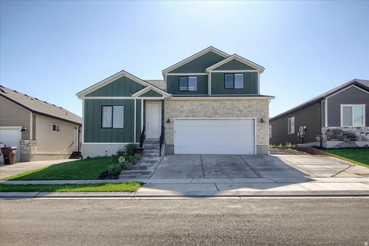Modern residential exterior featuring a two-story design with green vertical siding, stone veneer accents, and a white garage door