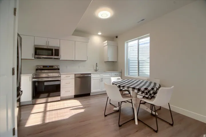 Contemporary kitchen featuring stainless steel appliances, white cabinetry, light-toned countertops, and wood-finish flooring