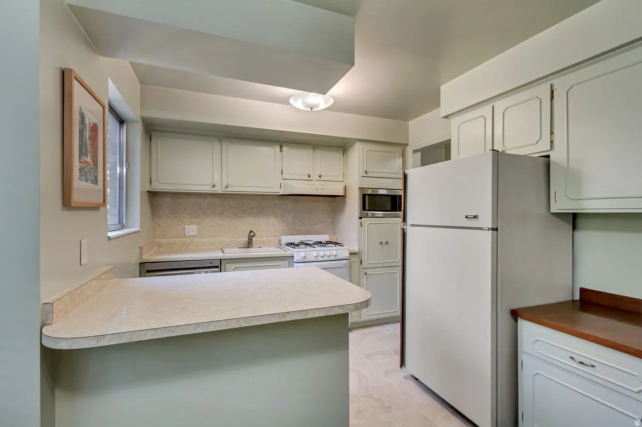 Kitchen featuring light cabinetry, a built-in microwave, a gas range, and a breakfast bar with a laminate countertop