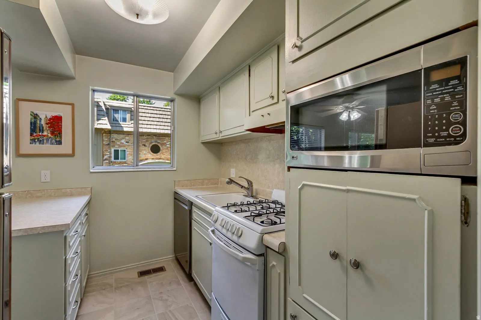 Kitchen featuring light-toned cabinetry, a stainless steel built-in microwave, a gas range, a single-basin sink, and a window providing natural light