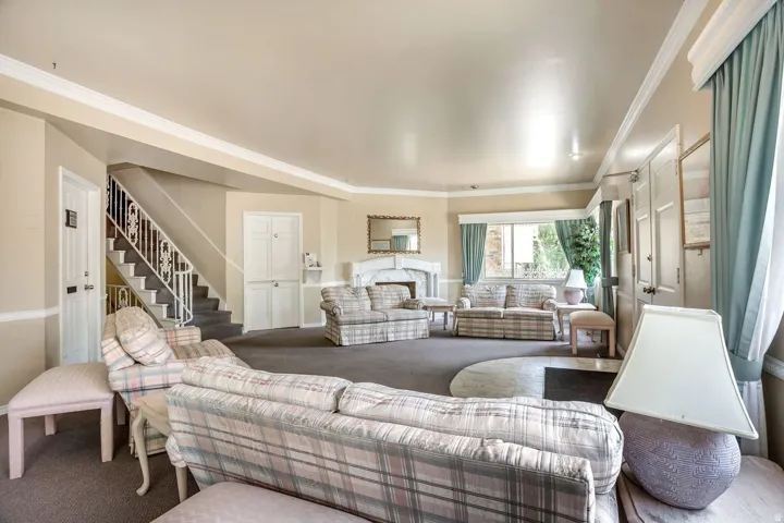 Sophisticated open-concept living area featuring soaring ceilings with recessed lighting, neutral plaid upholstered seating, wood-finish flooring throughout, large windows with sage green drapery, and a curved architectural layout