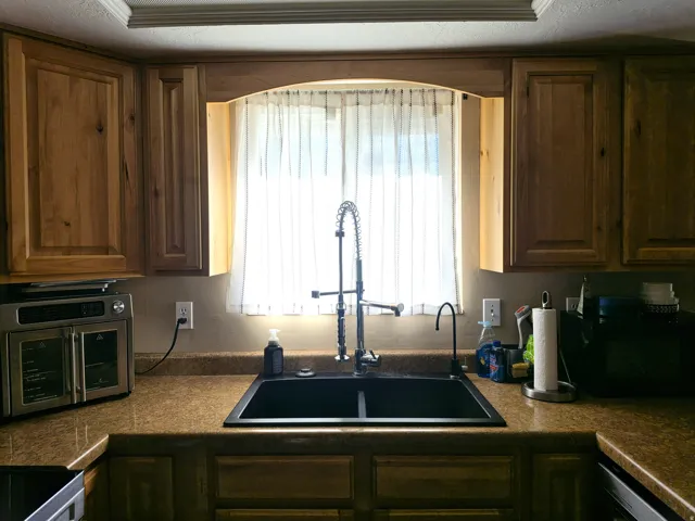 Kitchen features a double basin sink with a high-arc faucet, wood cabinetry, and a countertop with an integrated backsplash