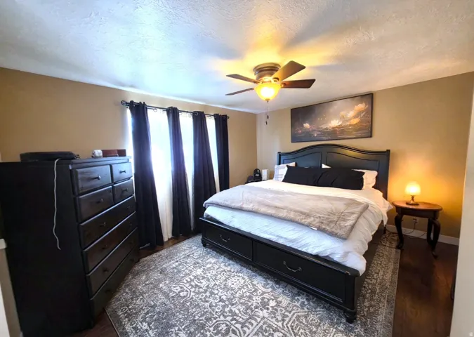 Spacious room featuring wood-finish flooring, a ceiling fan with integrated lighting, and multiple windows