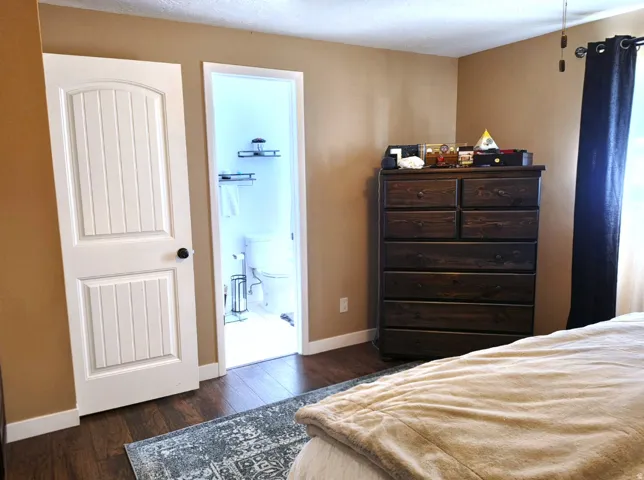 Wood-finish flooring throughout, featuring a white paneled door with black hardware, and a ceiling fan with wood-tone blades