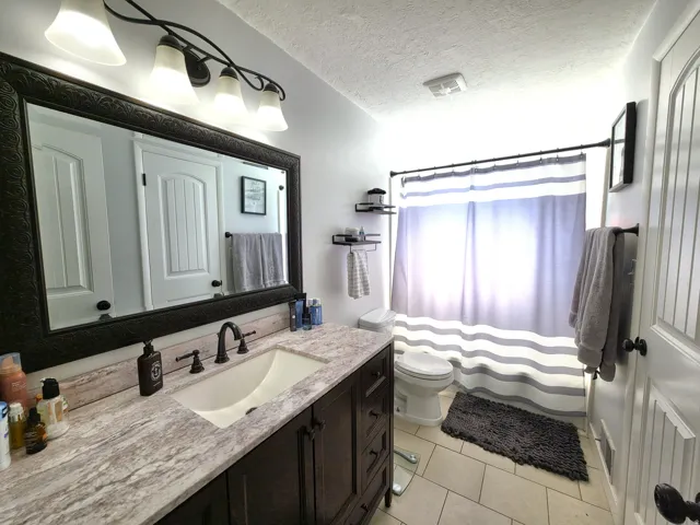 Spacious bathroom featuring a dark wood-finish vanity with an integrated sink, a generously sized framed mirror, and a coordinated four-light fixture