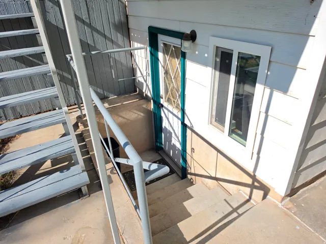 Exterior entry featuring a teal door with diamond-patterned security grating, an overhead wall lantern, and concrete steps with metal handrails