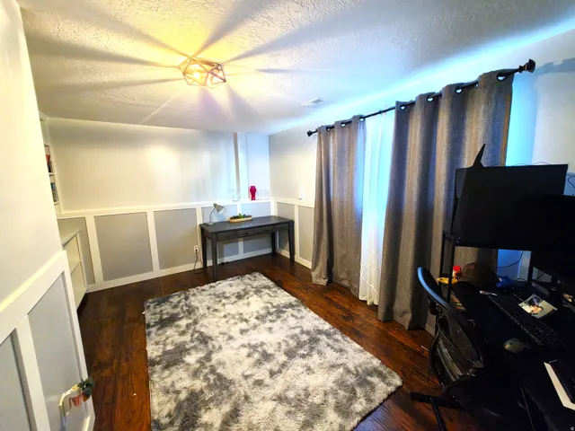 Room featuring dark wood-finish flooring, wainscoting, a modern geometric ceiling light fixture, and built-in shelving