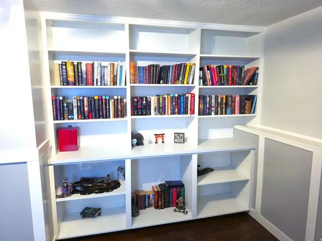 Custom built-in white shelving unit featuring crown molding and base trim, with a half-wall wainscoting detail