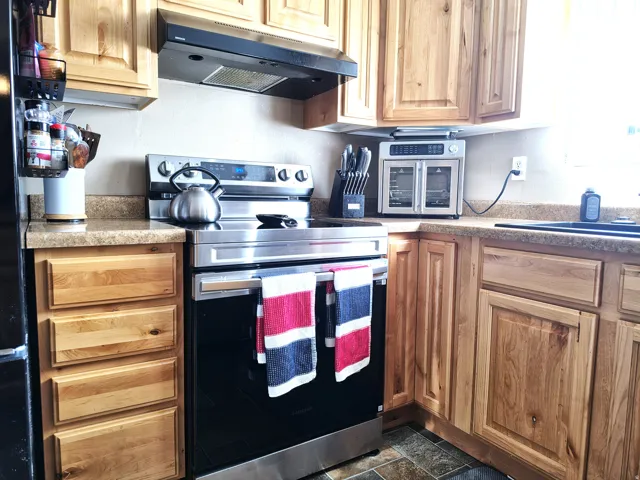 Kitchen featuring wood-finish cabinetry, solid surface countertops, a stainless steel electric range, and a black range hood