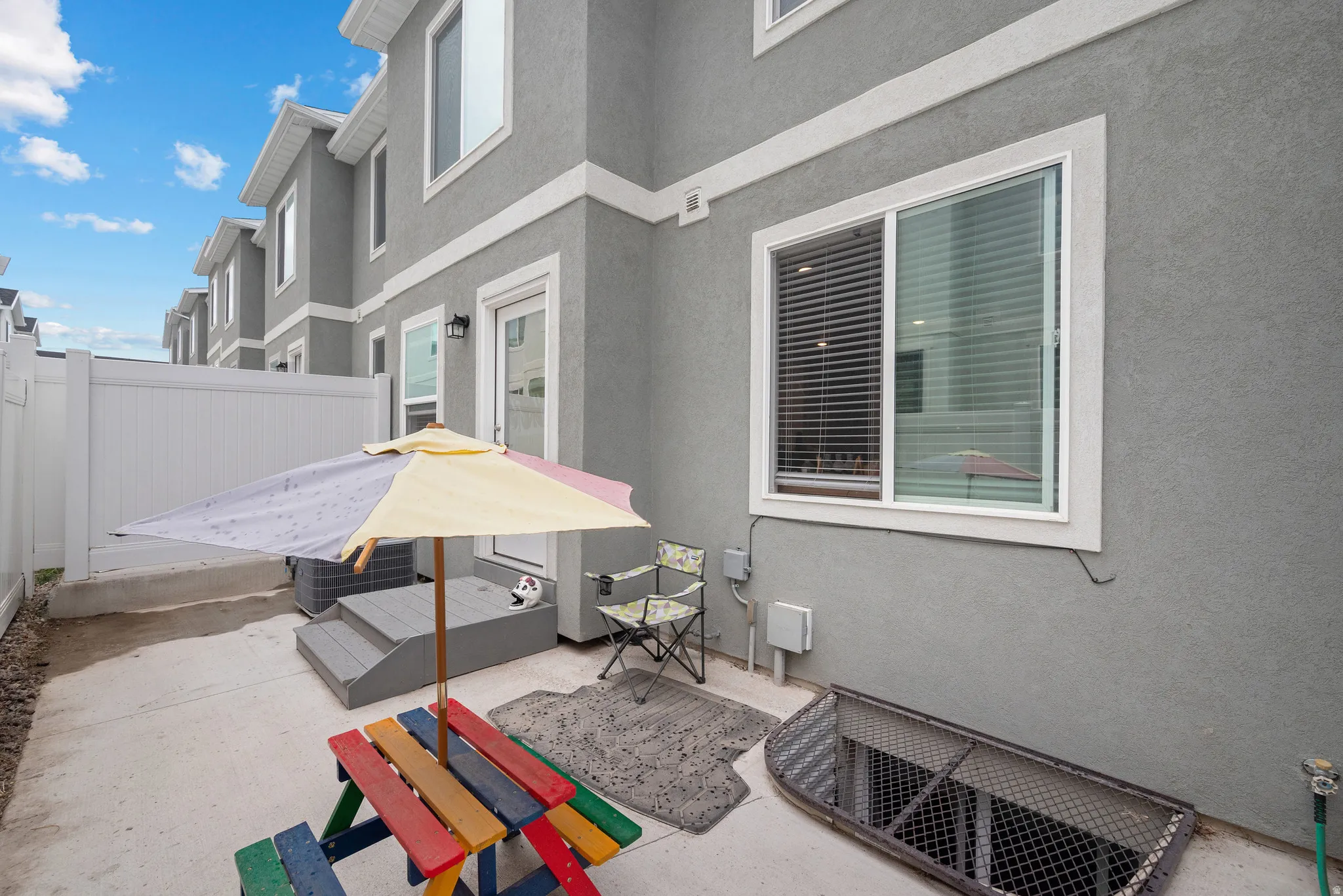 Private backyard patio retreat featuring a yellow market umbrella, comfortable seating area, and colorful play equipment on concrete patio