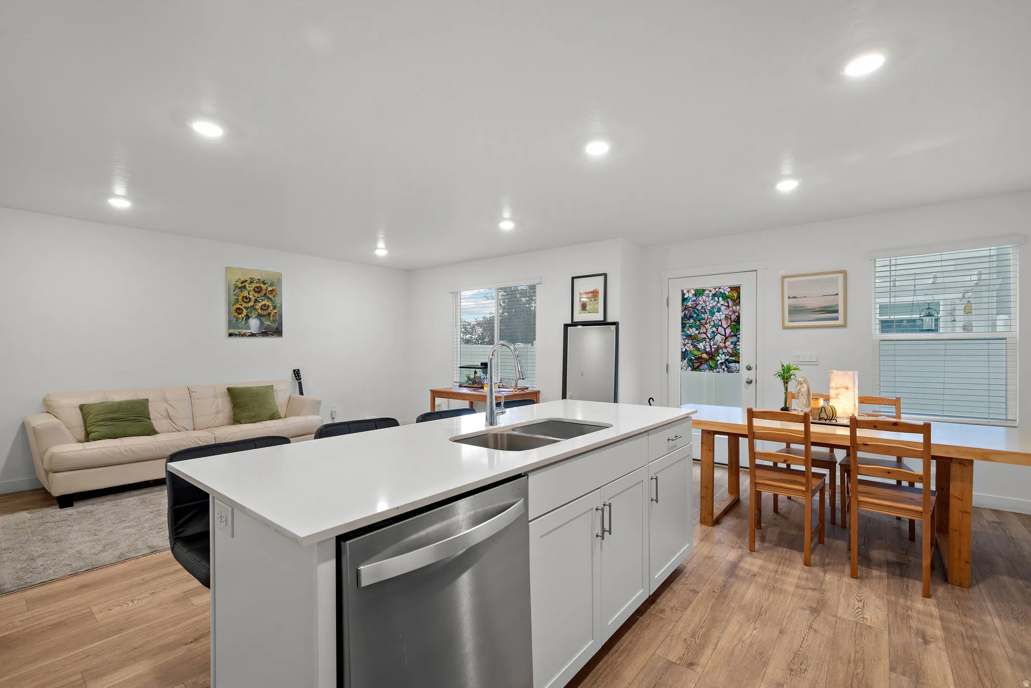 Open-concept kitchen and living area featuring a large white island with stainless steel appliances, white cabinetry, and wood-finish flooring