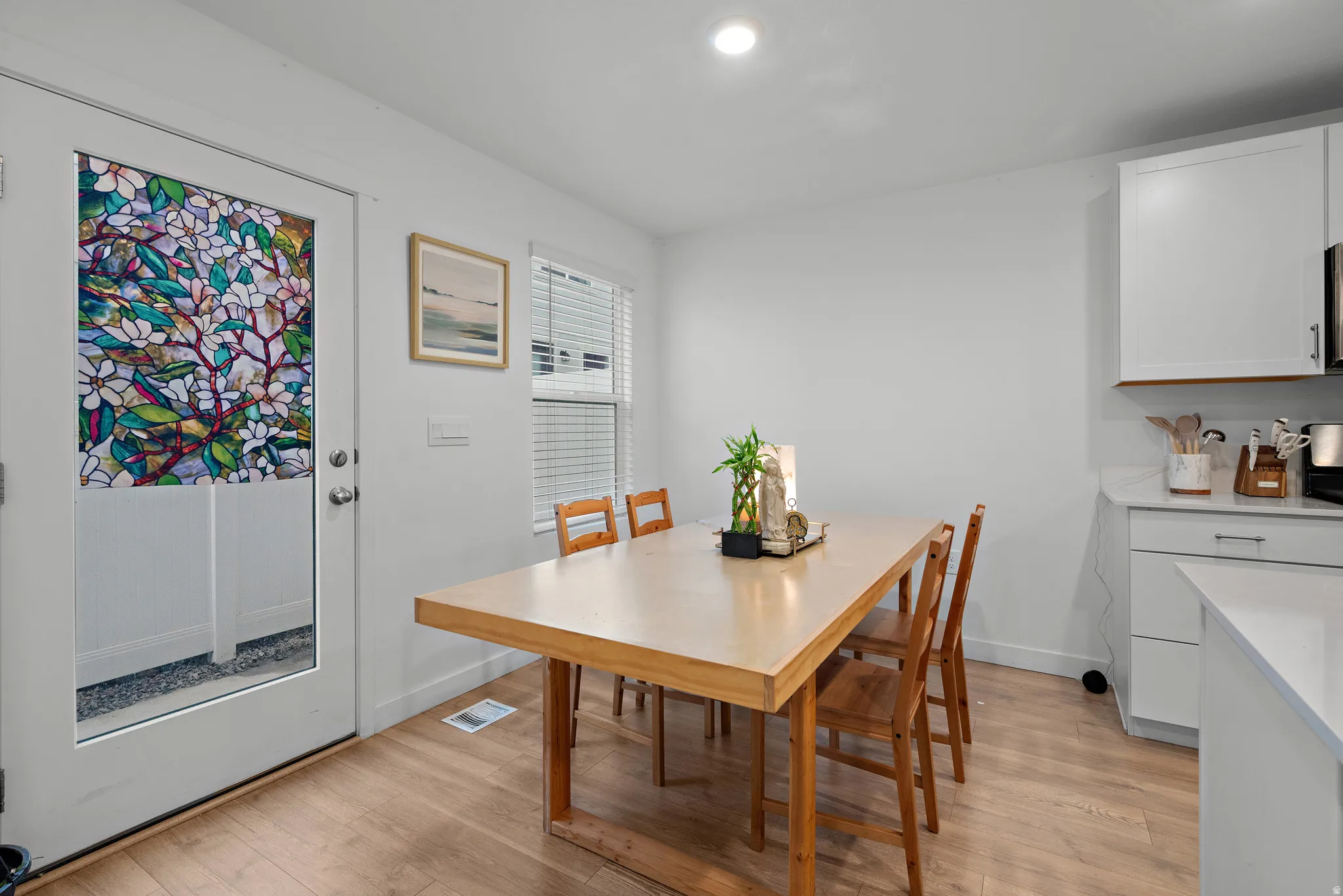 Bright dining area featuring a wood-finish table with seating for four, hardwood flooring, and abundant natural light from a glass door
