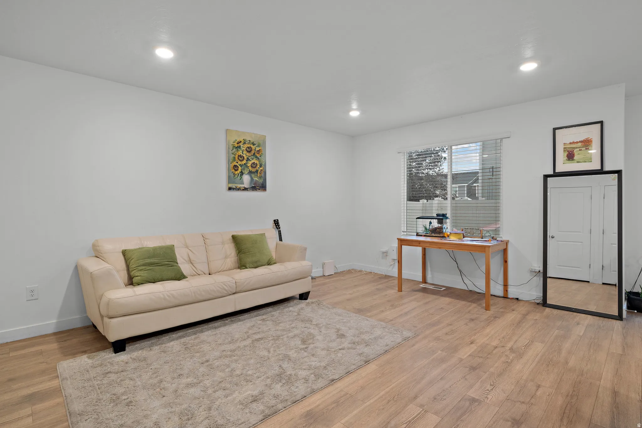 Bright and airy living space showcasing gleaming wood-finish flooring, recessed ceiling lighting, and neutral walls