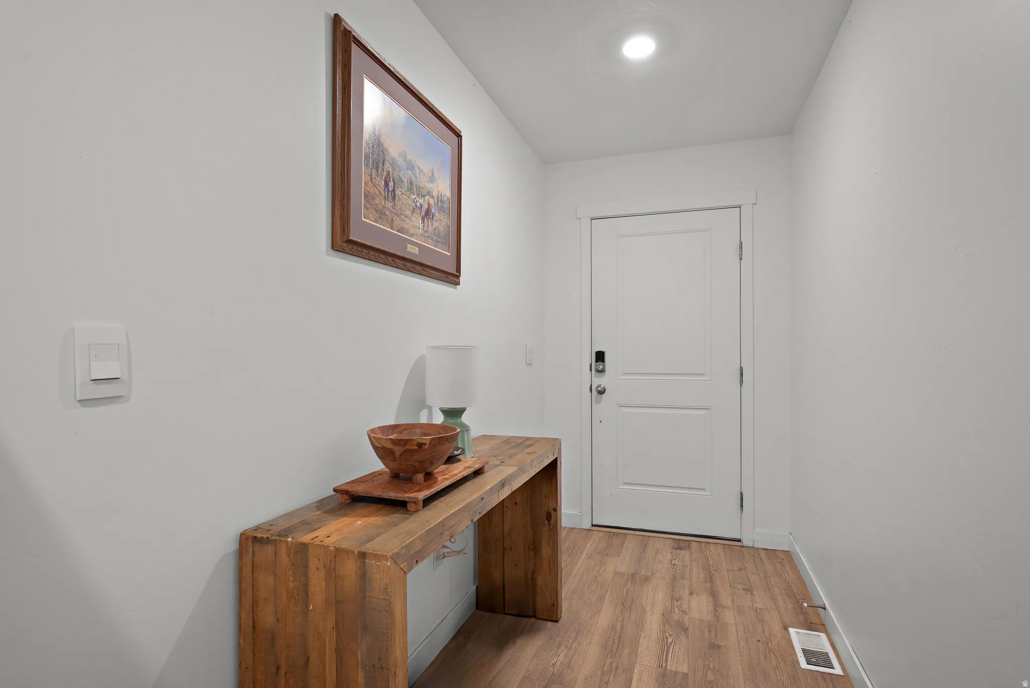 Welcoming entryway featuring warm wood-finish flooring, recessed ceiling lighting, and a custom wooden console table with decorative bowl and potted plant