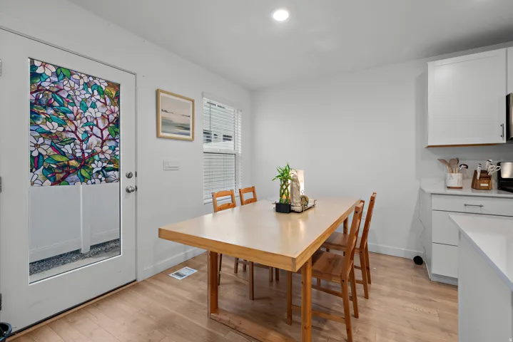 Bright dining area featuring a wood-finish table with seating for four, hardwood flooring, and abundant natural light from a glass door