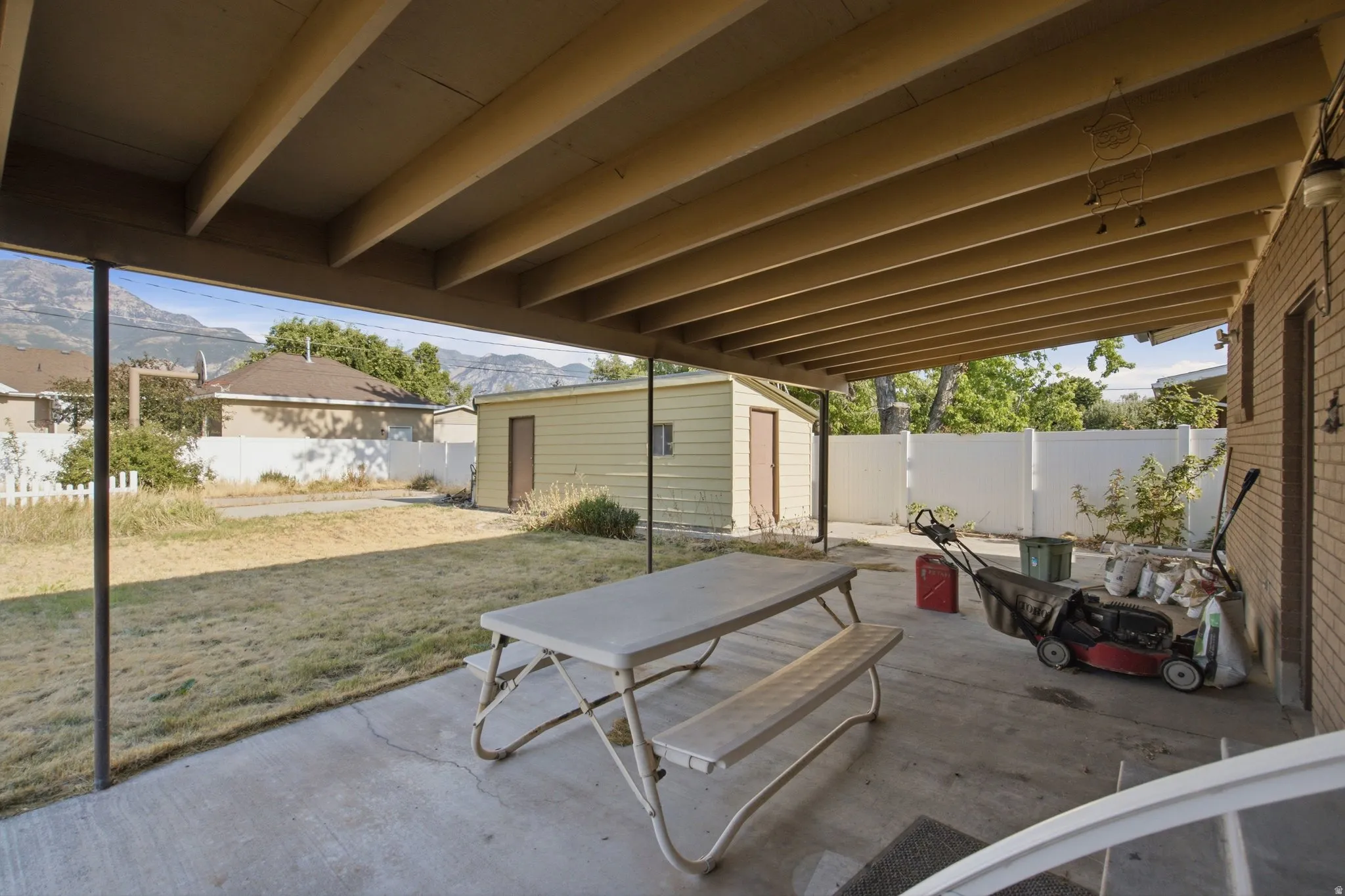 Covered concrete patio with exposed beam ceiling, brick exterior wall, and mountain backdrop