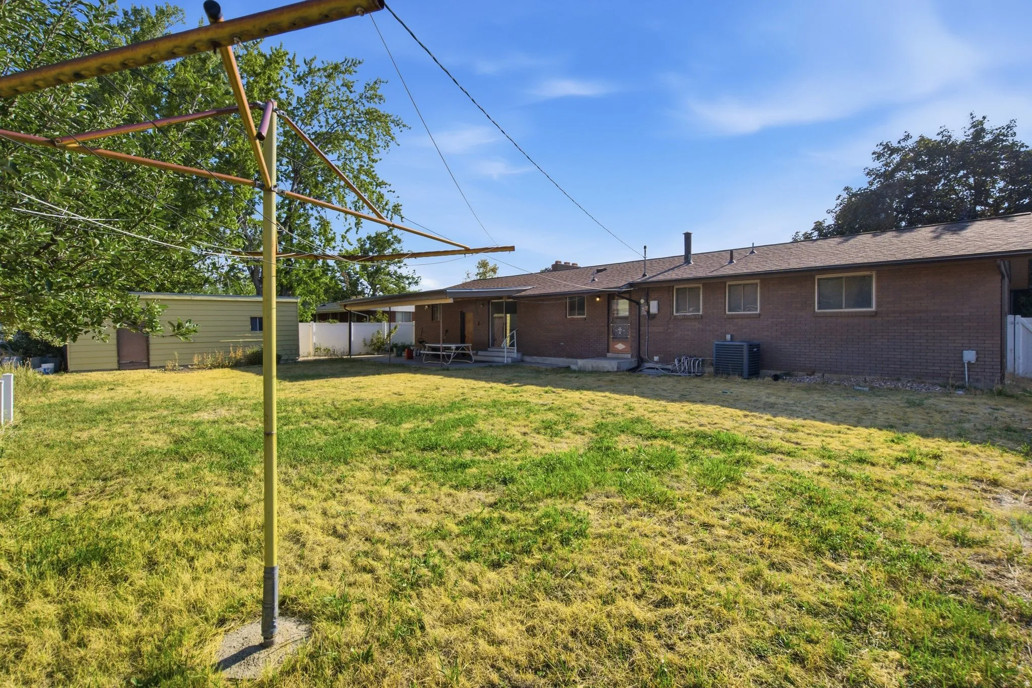 Expansive backyard featuring a single-story brick exterior, multiple windows, a rear entry door, and a detached shed