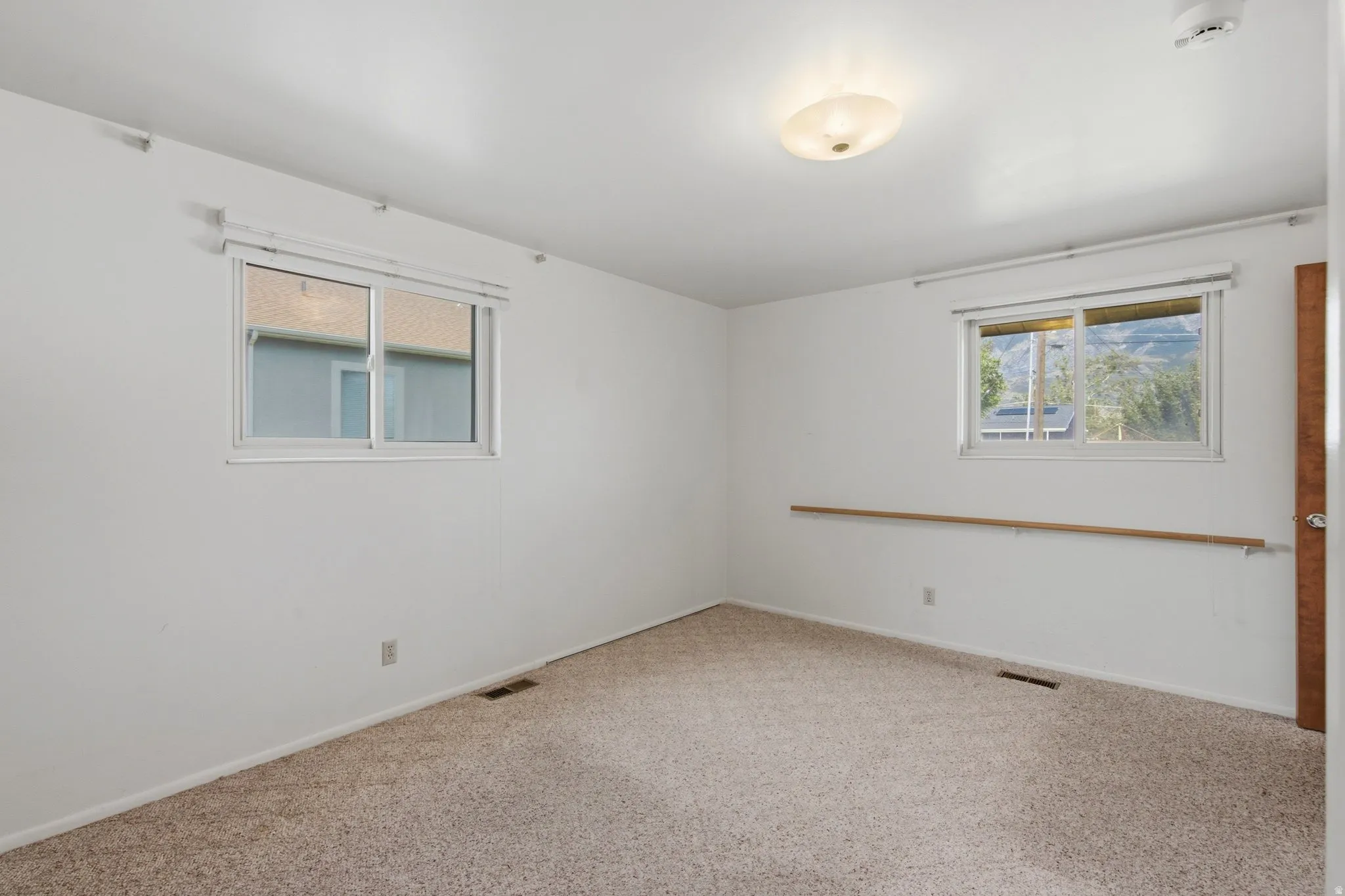 Spacious bedroom offering abundant natural light from dual windows, neutral carpeting, and clean white walls with wood-trim accents