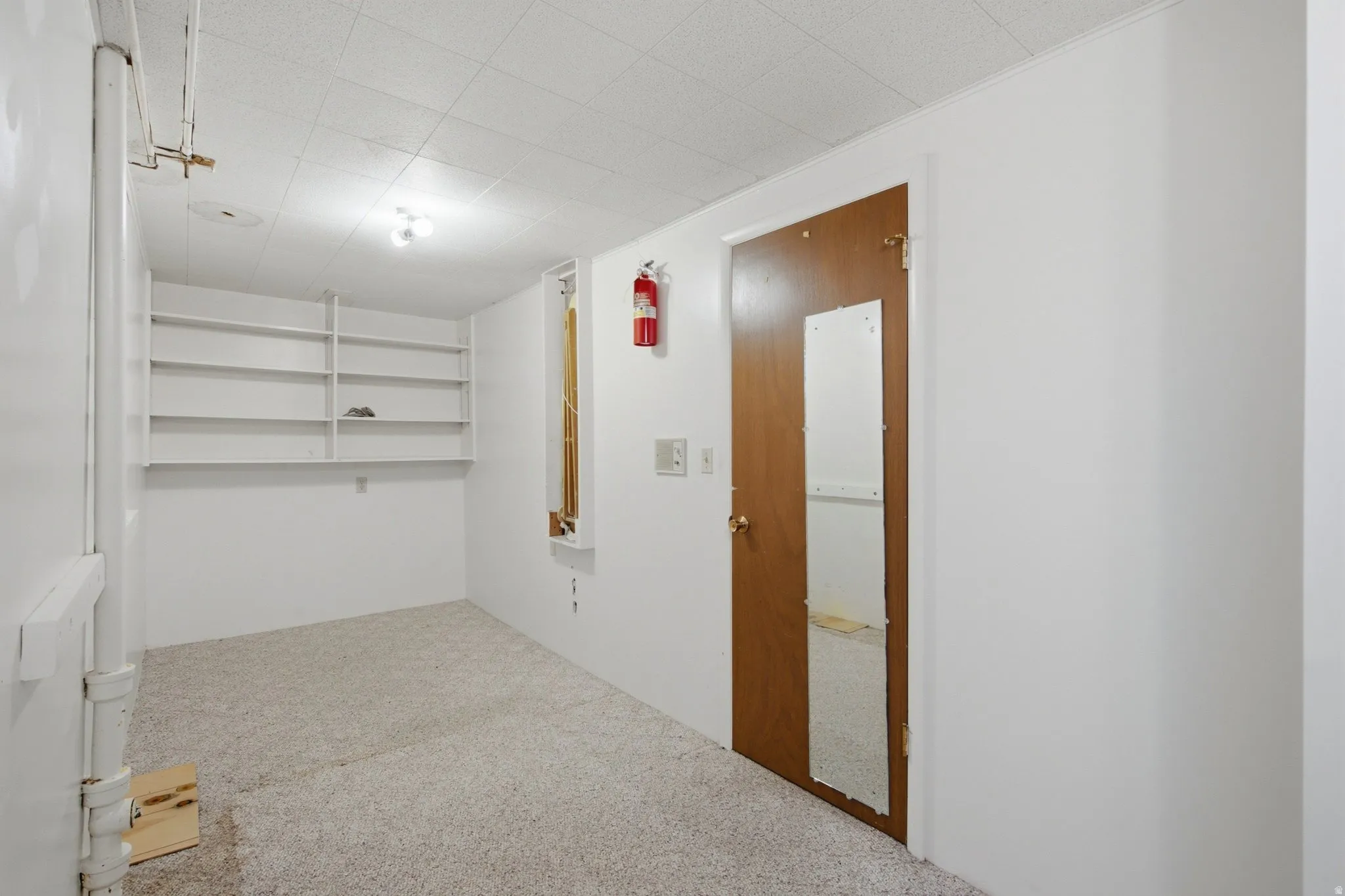 Carpeted room featuring built-in shelving, white walls, and a dropped ceiling with recessed lighting
