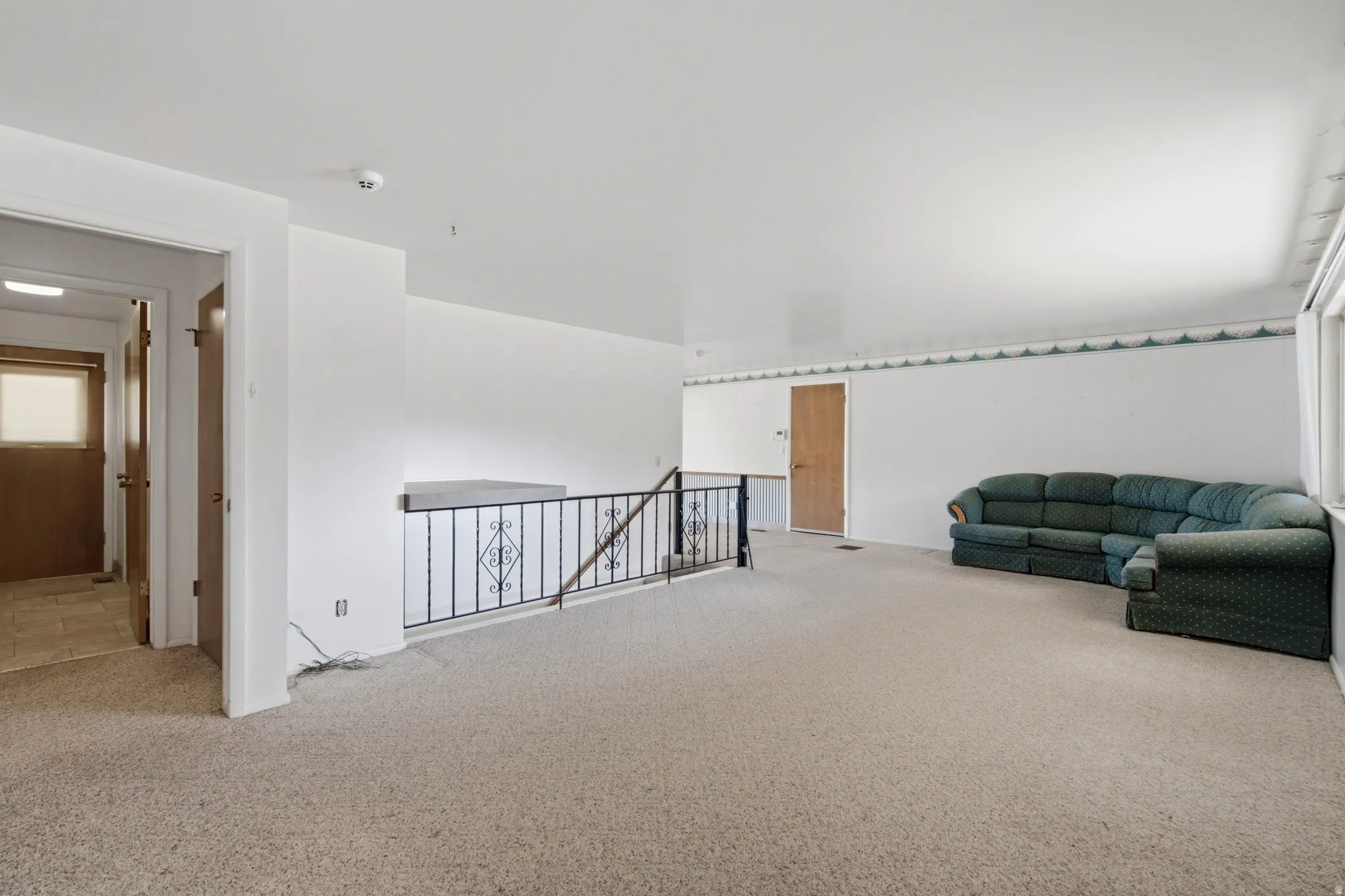 Carpeted upper-level space featuring a black iron railing, white walls, and a light wood-tone door