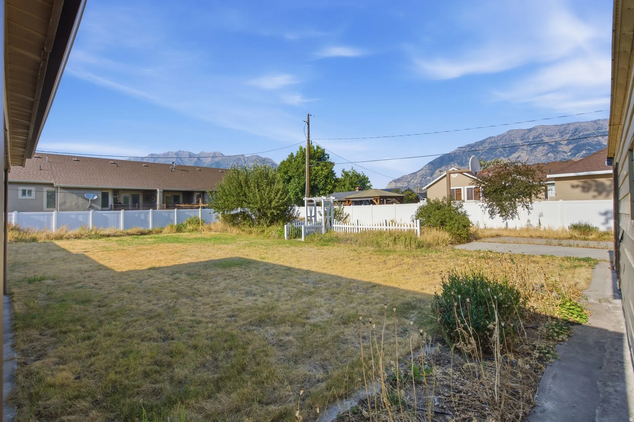 Expansive backyard featuring a partial white picket fence, a full privacy fence, and distant mountain scenery