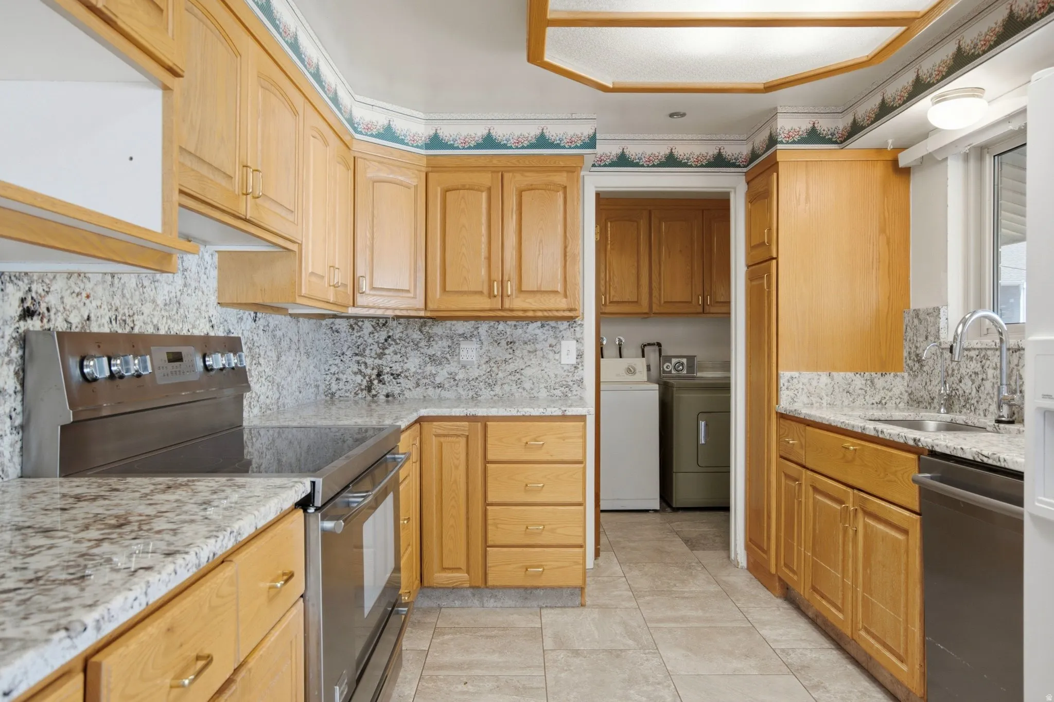 Galley-style kitchen featuring natural wood cabinetry with ample storage, granite-look countertops, stainless steel appliances including a double wall oven and built-in refrigerator, decorative tile backsplash, recessed ceiling lighting, and ceramic tile