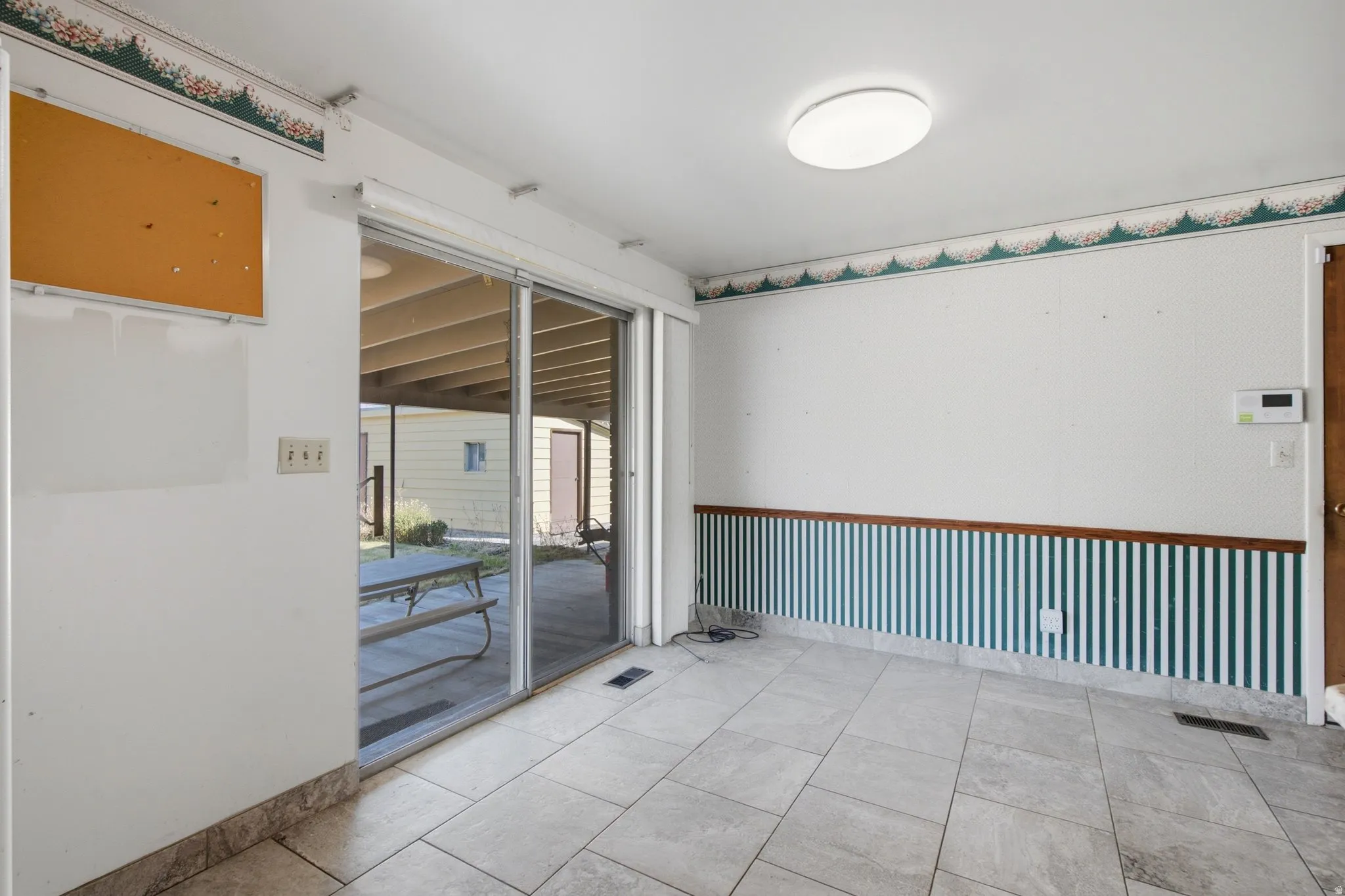 Spacious room featuring light-toned tile flooring, a large sliding glass door, and a flush-mount ceiling light