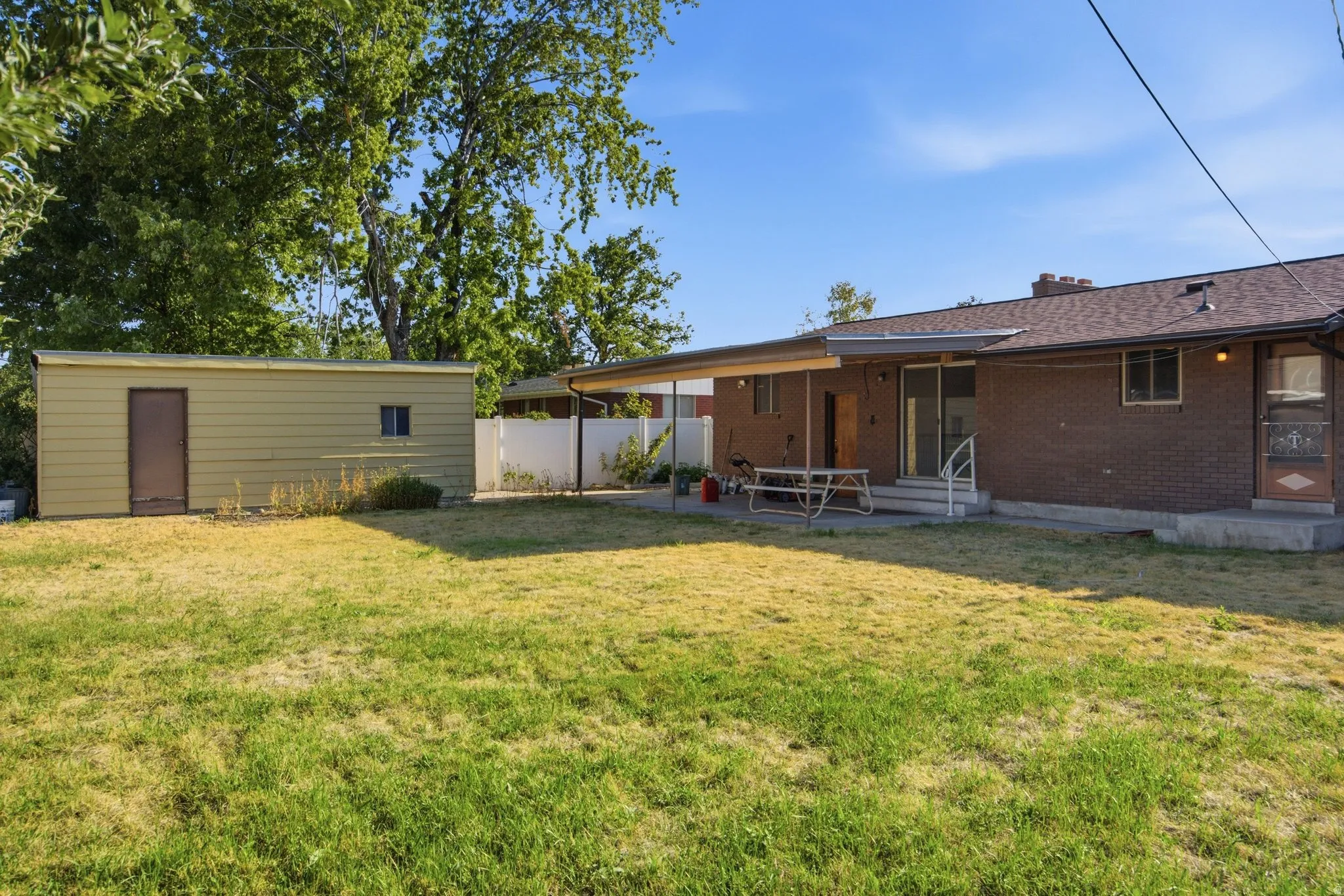 Expansive backyard featuring a detached storage shed, a covered patio, and a brick-clad exterior