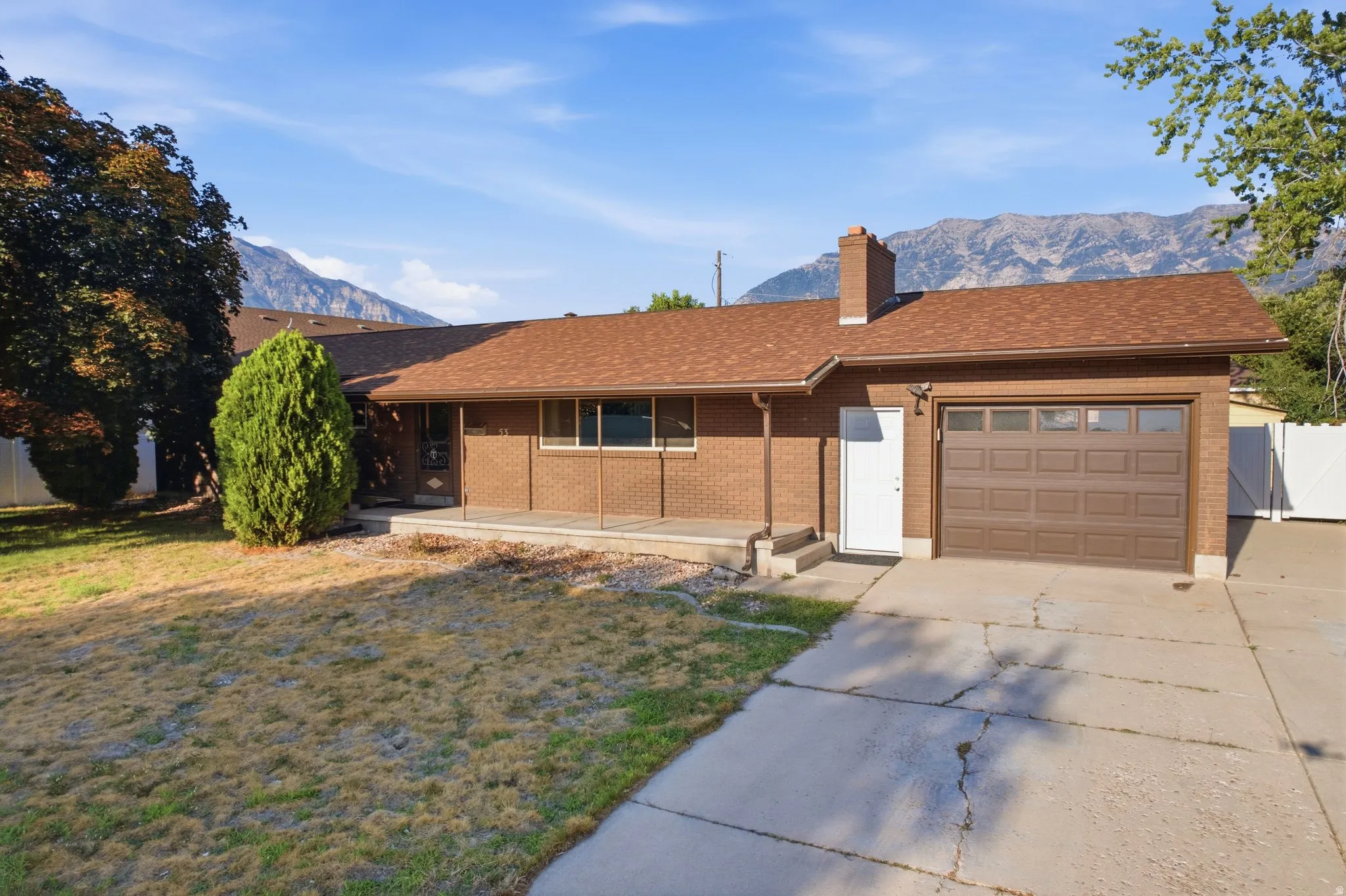 Traditional brick exterior with an attached garage, a brown shingle roof, and a mature tree
