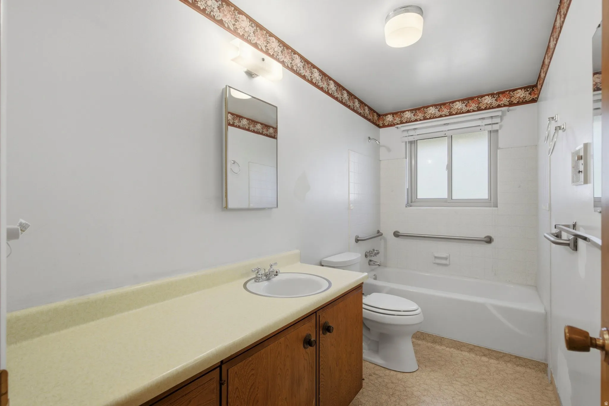 Bathroom featuring a wood vanity with integrated sink, white tub with tiled surround, and window with blinds