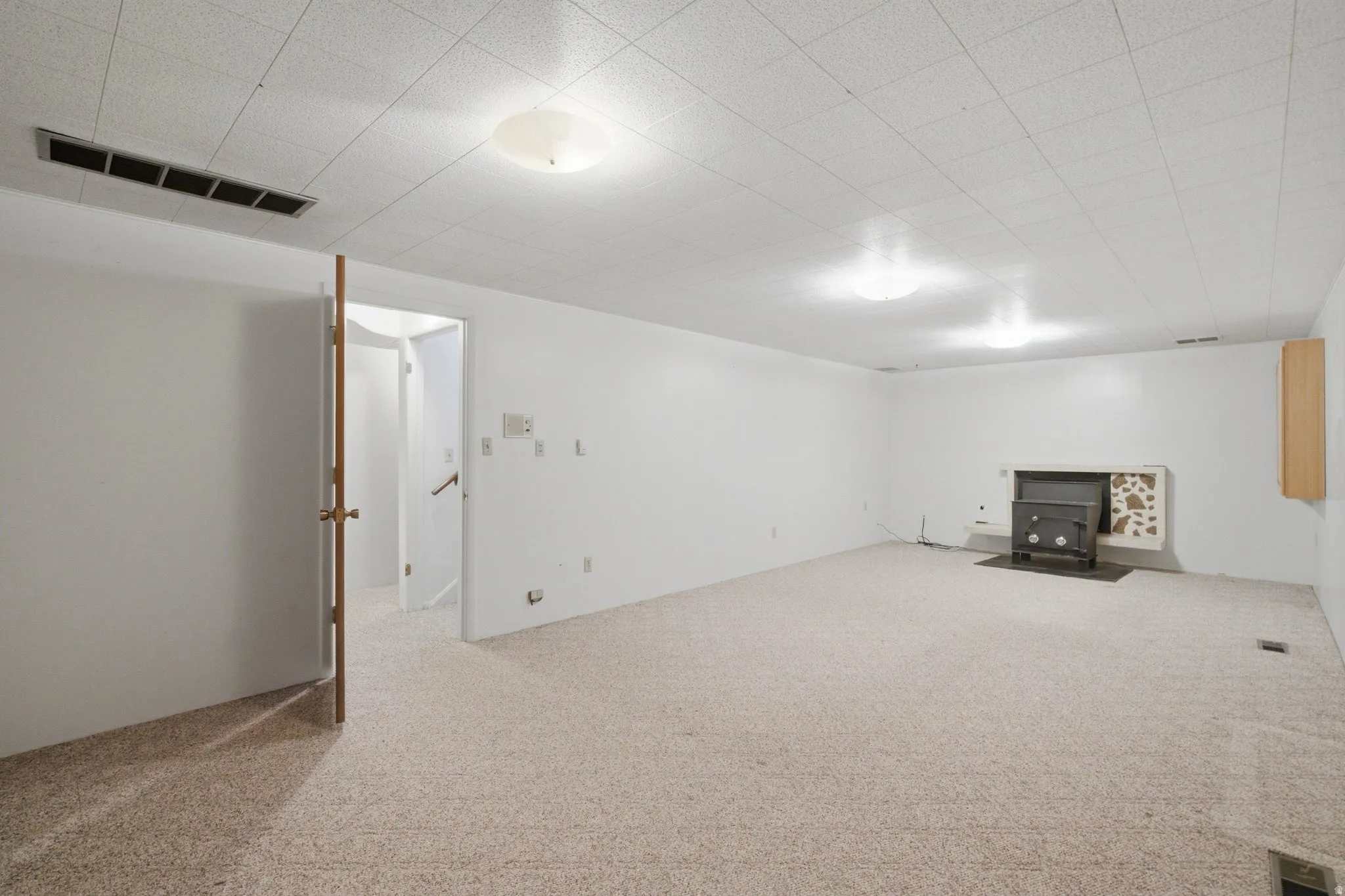 Spacious room featuring light-colored carpet flooring, recessed ceiling tiles, and flush-mount lighting fixtures