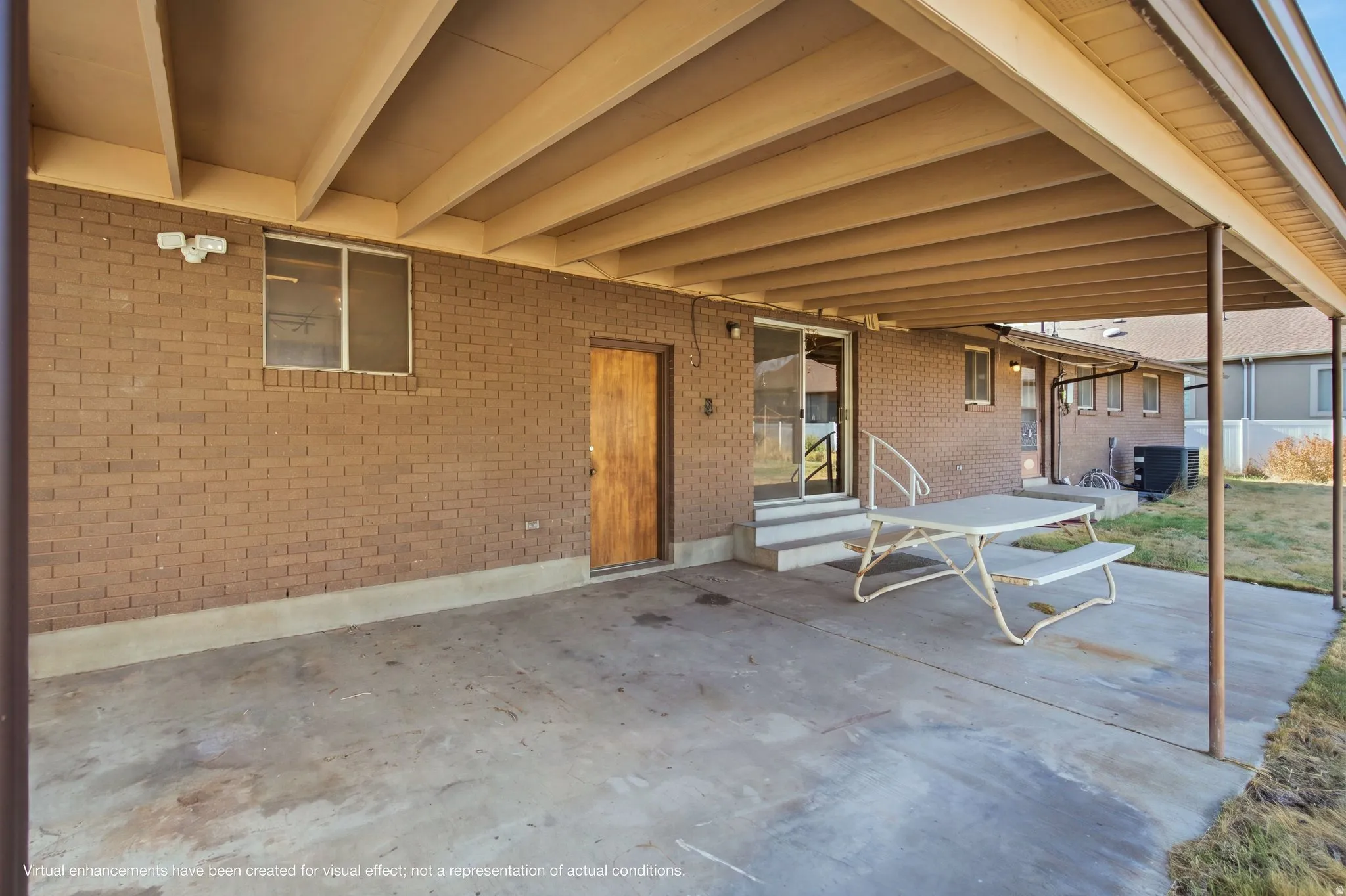 Expansive covered patio featuring a concrete foundation, exposed beam ceiling with wood-finish detailing, and brick exterior
