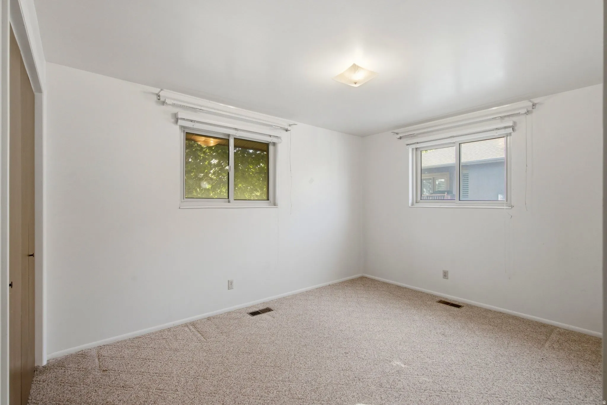 Carpeted room featuring two windows with blinds, a flush mount ceiling light fixture, and a light wood-finish door