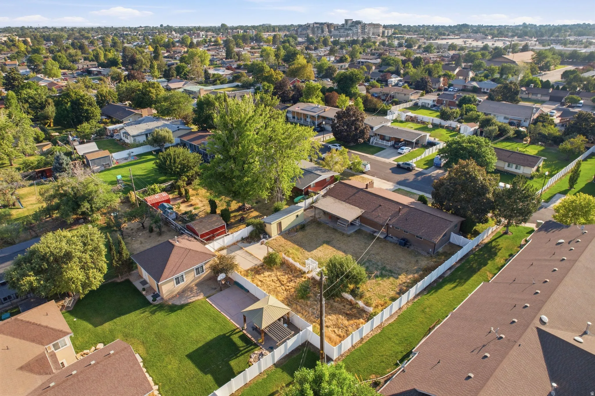 Expansive property featuring a detached residence, a large grassy lawn, a covered patio area, and a white picket fence