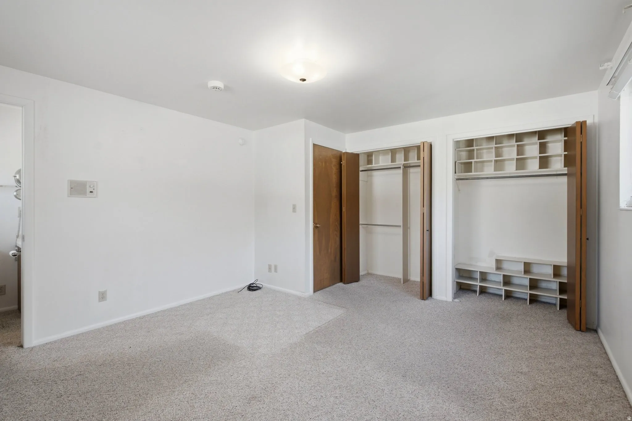 Carpeted room featuring two bifold door closets with built-in shelving and hanging rods, white walls, and a flush-mount ceiling light fixture