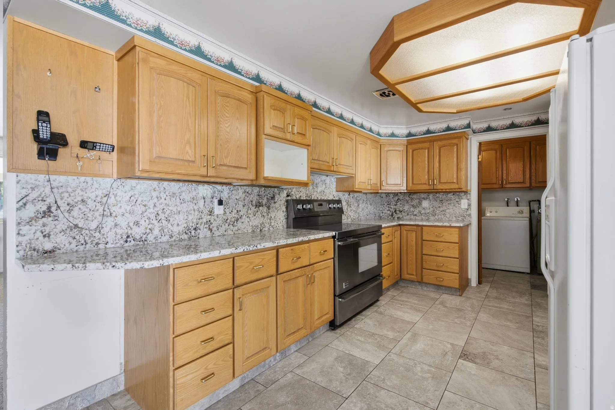 Kitchen featuring light wood cabinetry, stone-finish countertops, stainless steel range, and tile flooring