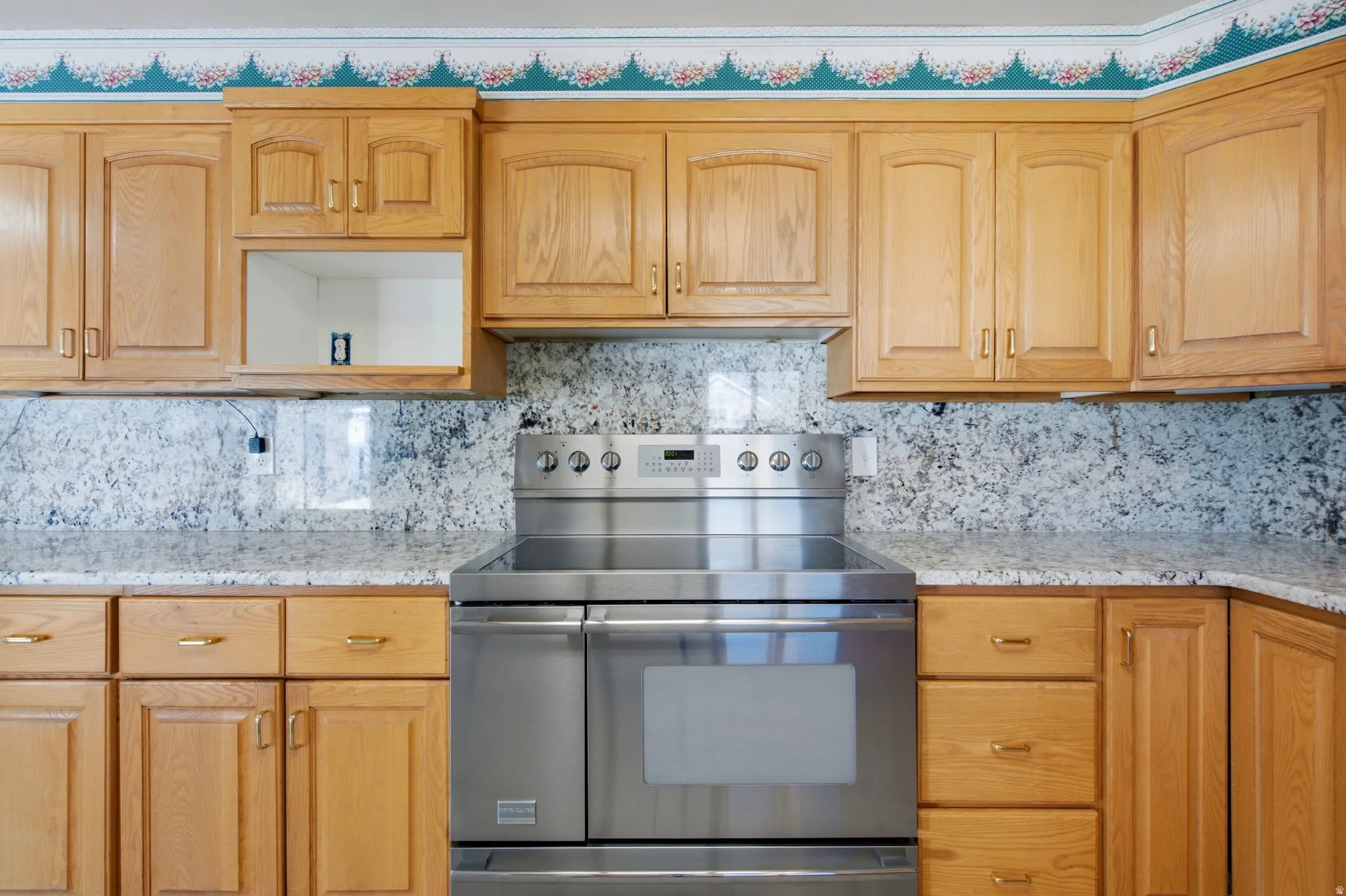 Kitchen featuring a stainless steel electric range, light wood-finish cabinetry, and speckled countertops