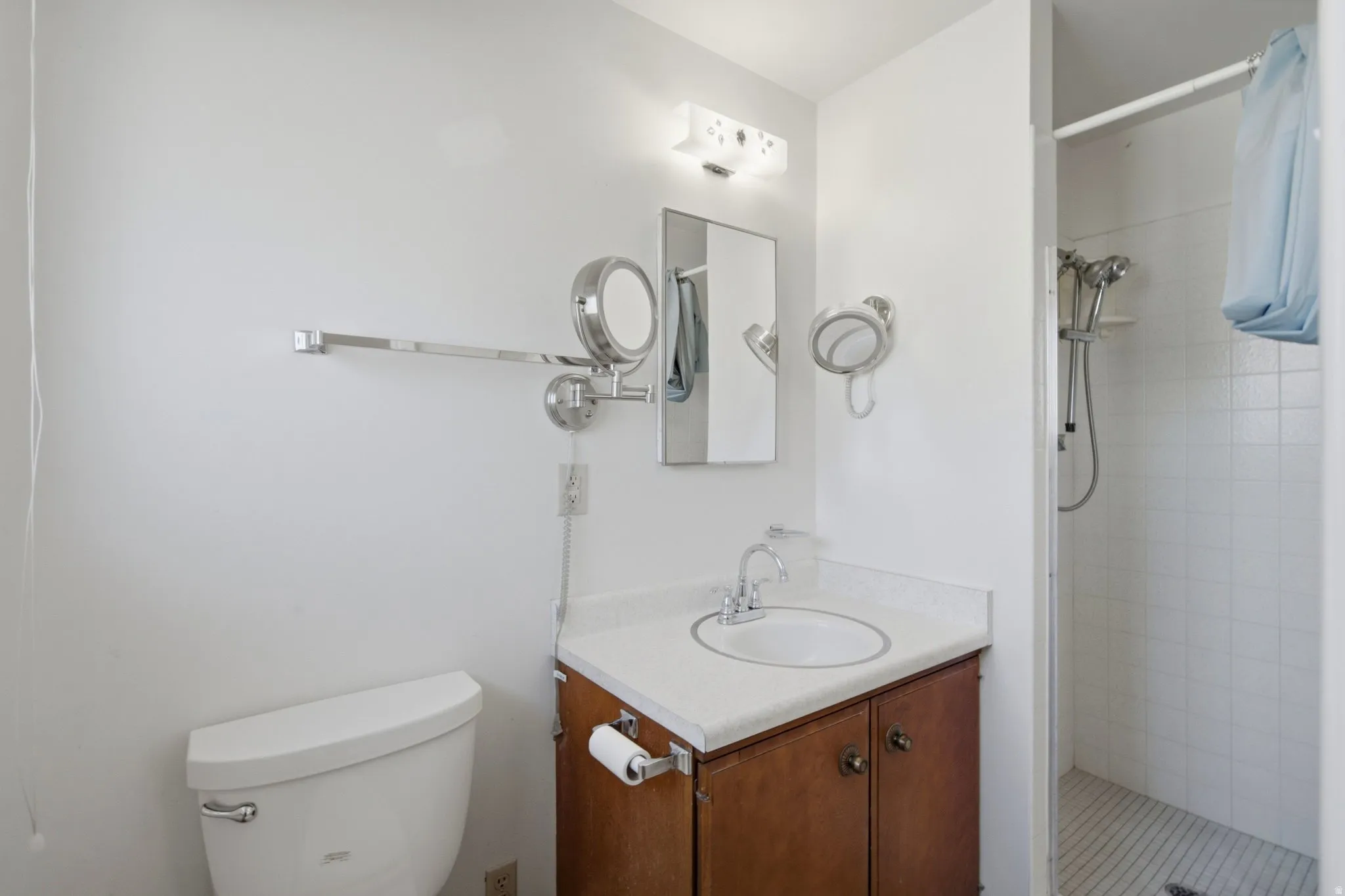 Bathroom featuring a vanity with a white countertop and wood-finish cabinetry, a toilet, and a tiled shower with a handheld shower fixture