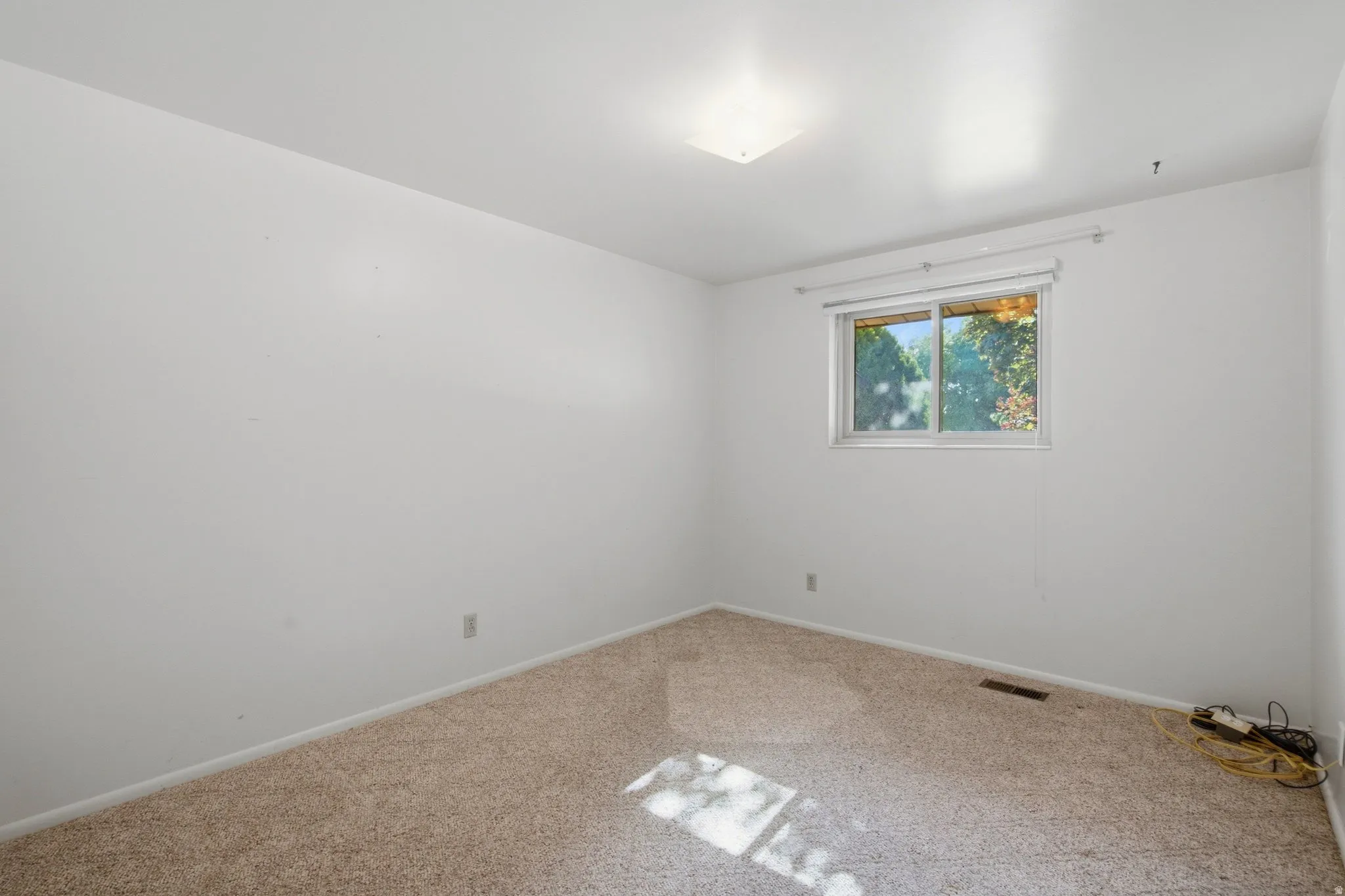Carpeted room with white walls, a single window, and an overhead light fixture