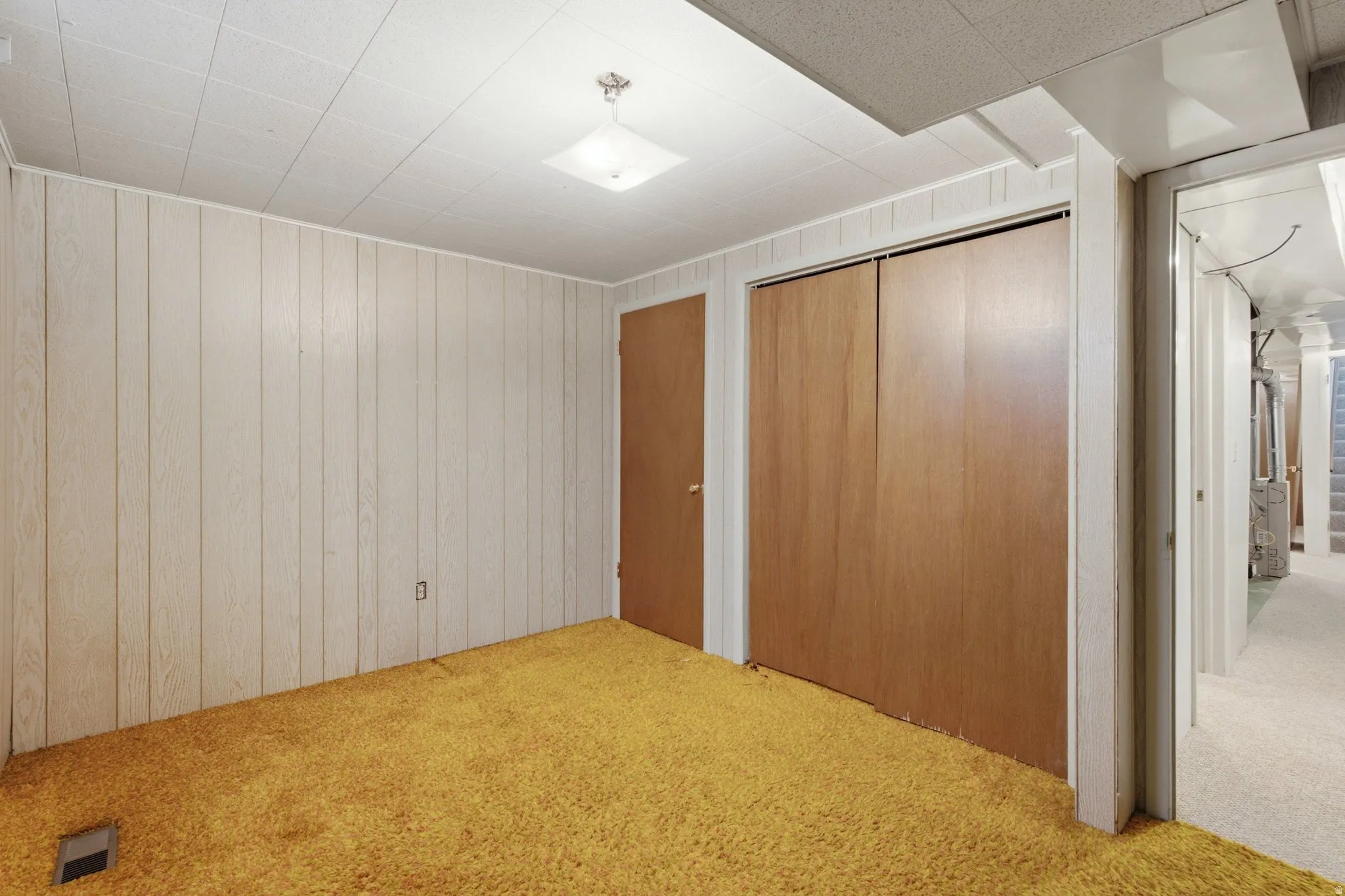 Spacious carpeted room featuring neutral paneled walls, wood-finish doors with white trim, recessed ceiling lighting, and direct access to hallway spaces