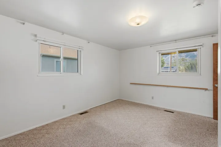 Spacious bedroom offering abundant natural light from dual windows, neutral carpeting, and clean white walls with wood-trim accents