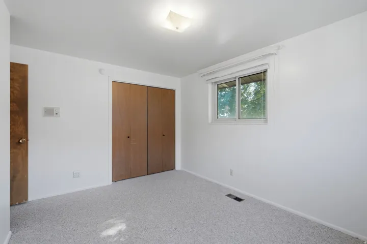 Bedroom with light gray carpeting, neutral white walls, and a window featuring a white-framed casement