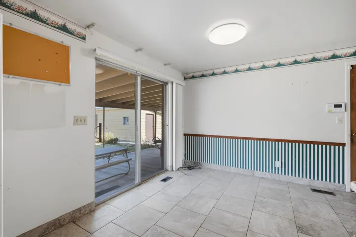 Spacious room featuring light-toned tile flooring, a large sliding glass door, and a flush-mount ceiling light