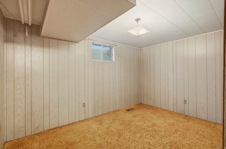 Room with light-toned vertical paneling, a textured ceiling, and a single window