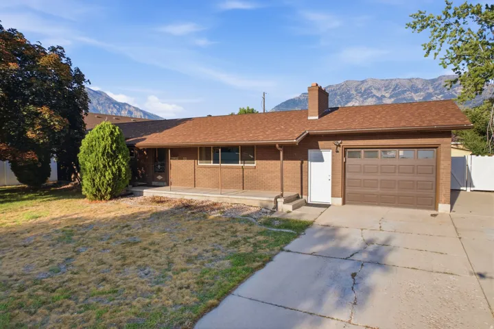 Traditional brick exterior with an attached garage, a brown shingle roof, and a mature tree